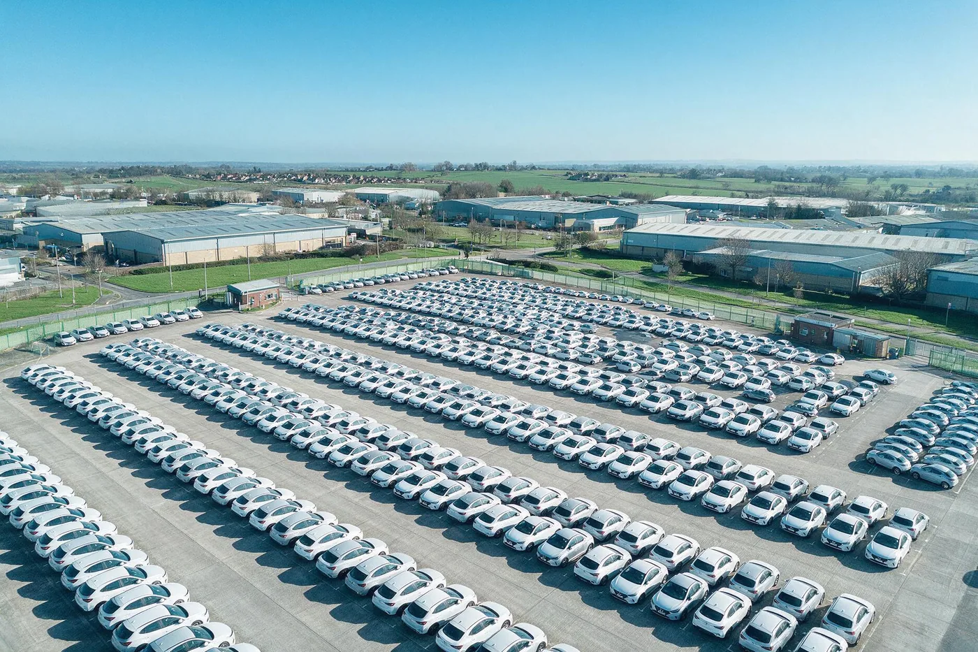 Aerial view of hundreds of new cars parked in rows at a vehicle storage compound